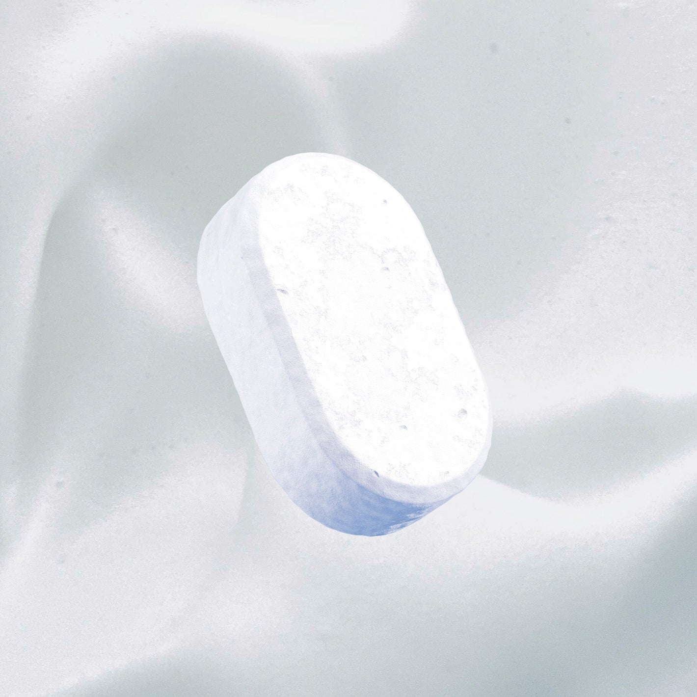 A single white, oval tablet hovers over a smooth white background, reflecting the simplicity of fragrance-free dishwasher detergent.