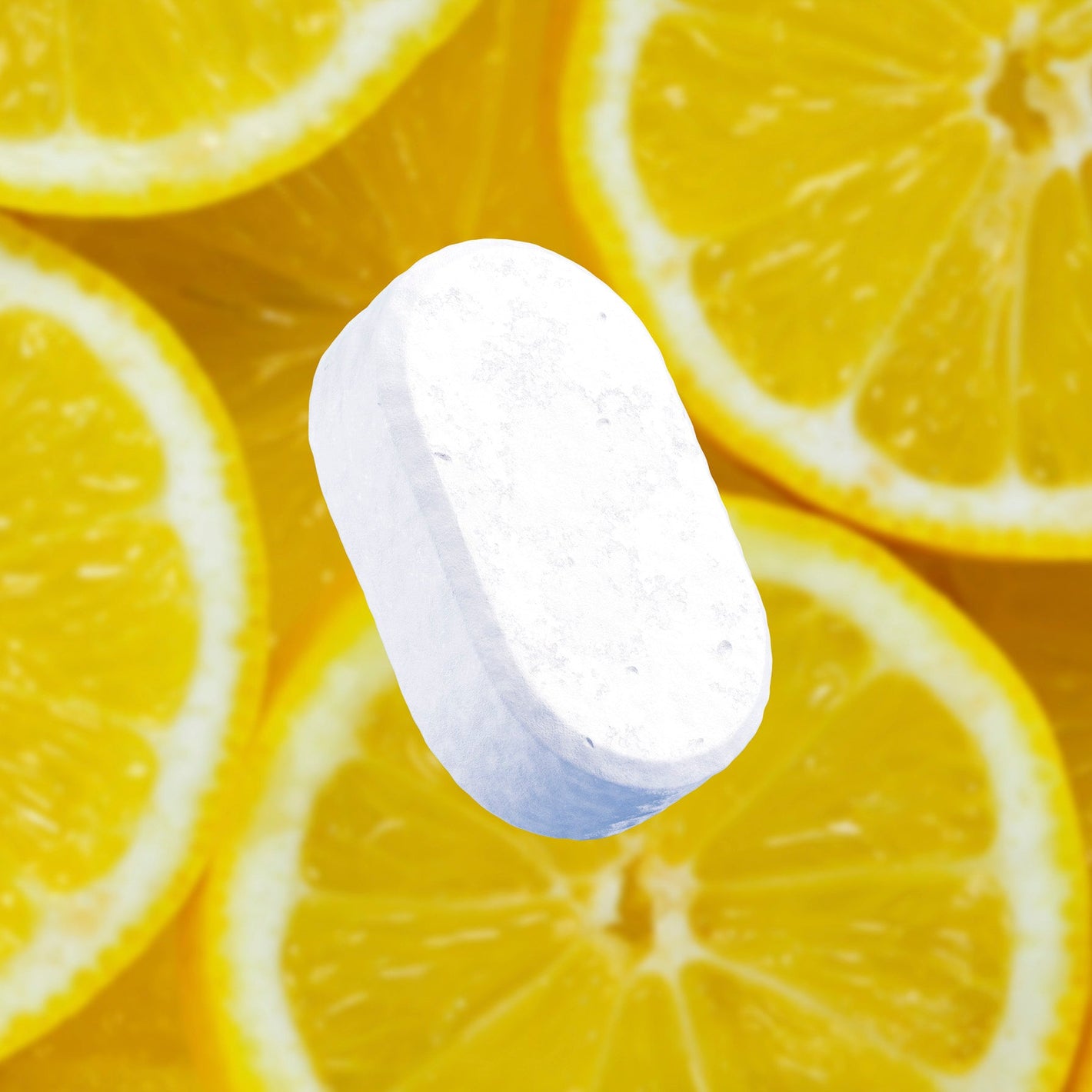 A white, oval tablet sits atop vibrant yellow lemon slices.